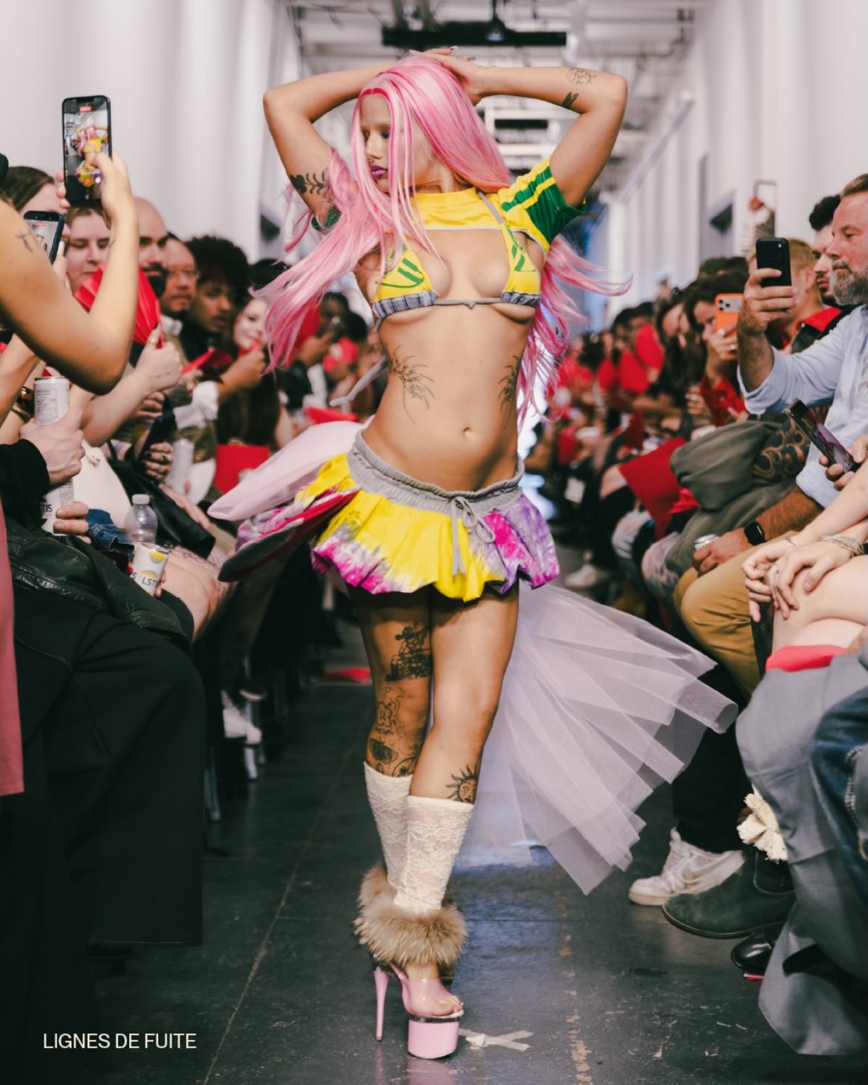 Une personne aux cheveux roses porte une tenue jaune et verte sur le podium d’ON SHOW pendant la Semaine de la mode de Montréal.