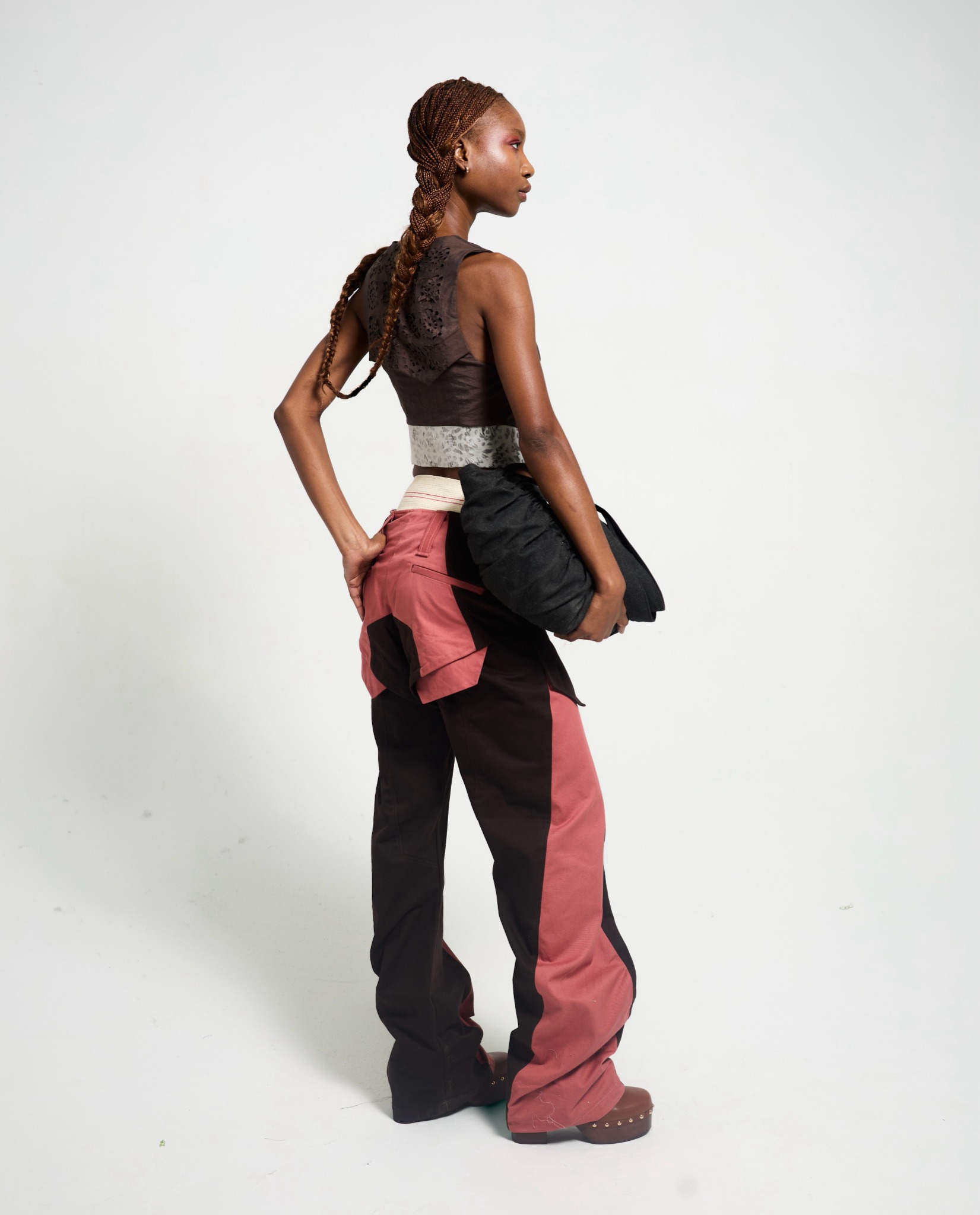 OSČ lookbook: back view of a dark vest and black and rose trousers with a dark bag.