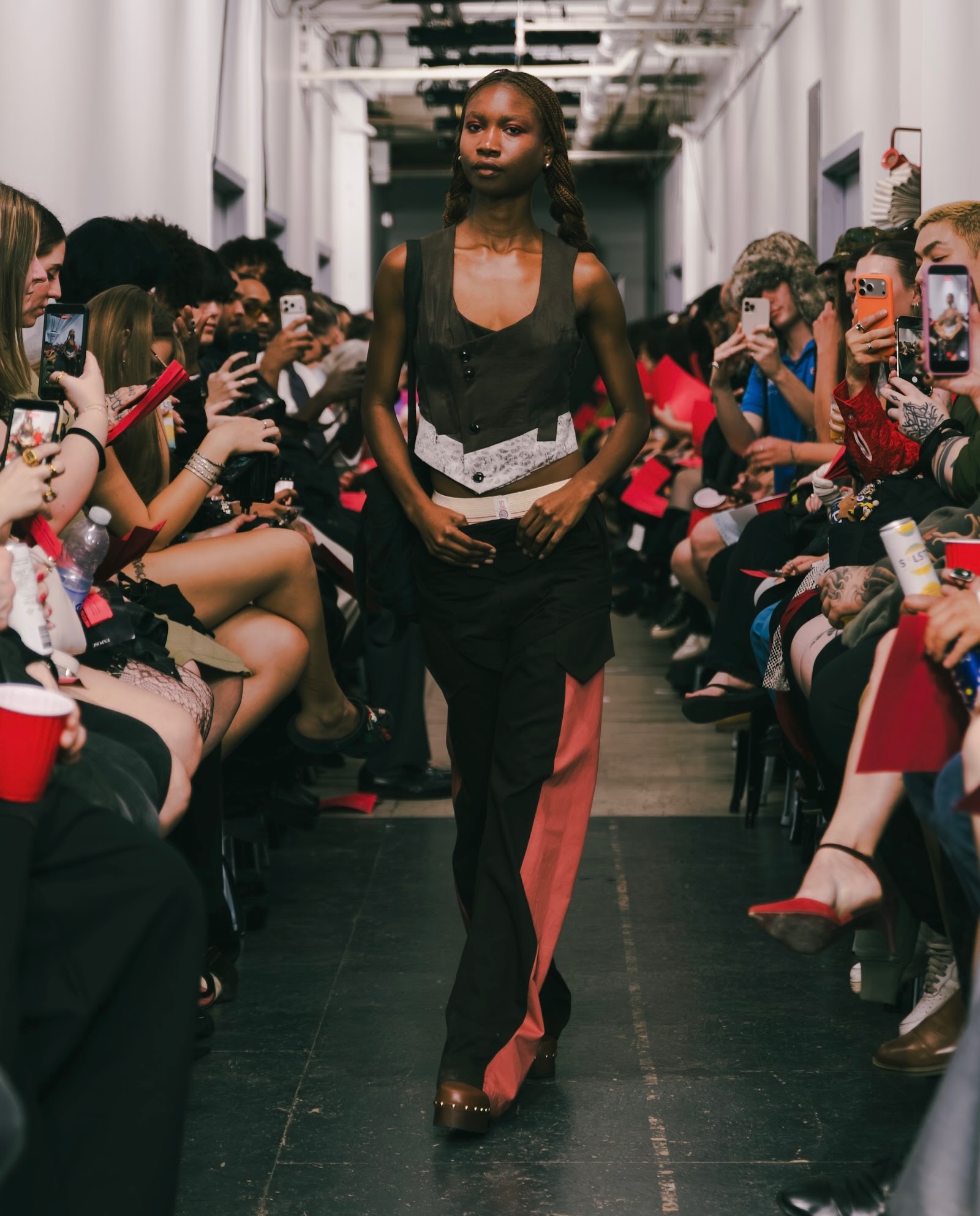 OSČ runway look: a dark fitted vest with a pale patterned hem and black and rose trousers.