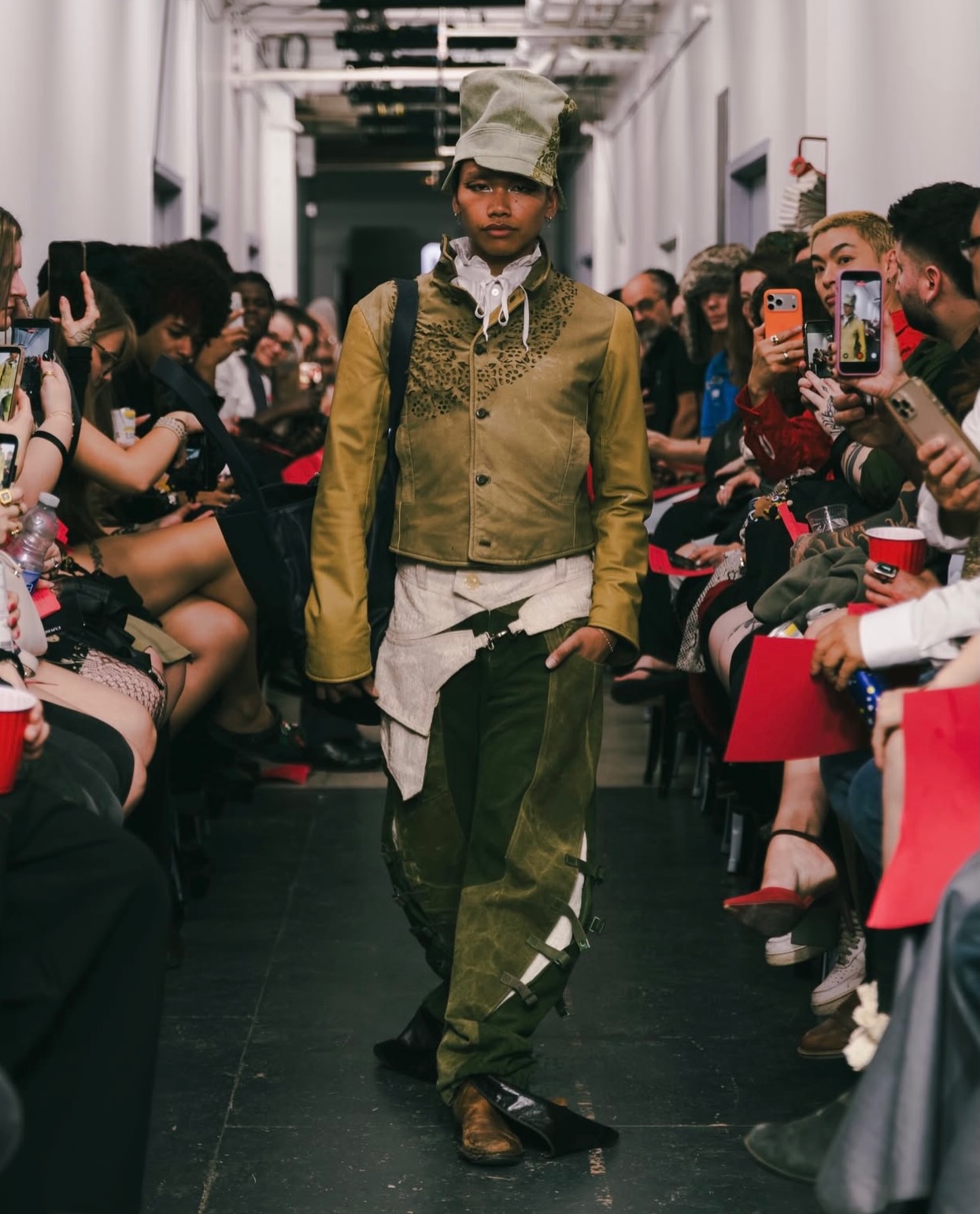 OSČ runway look: a green cap, cutwork jacket and buckled trousers.