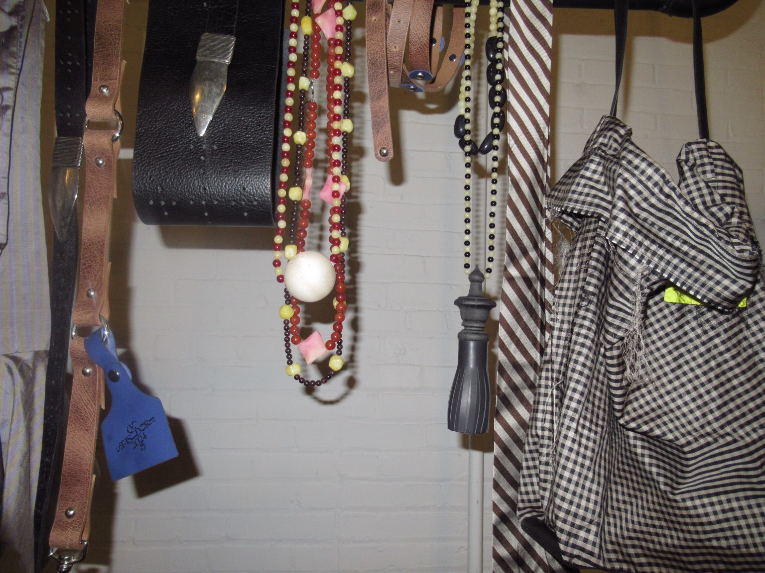 Colliers de perles, accessoires en cuir, cravate rayée et vêtement à carreaux présentés ensemble.
