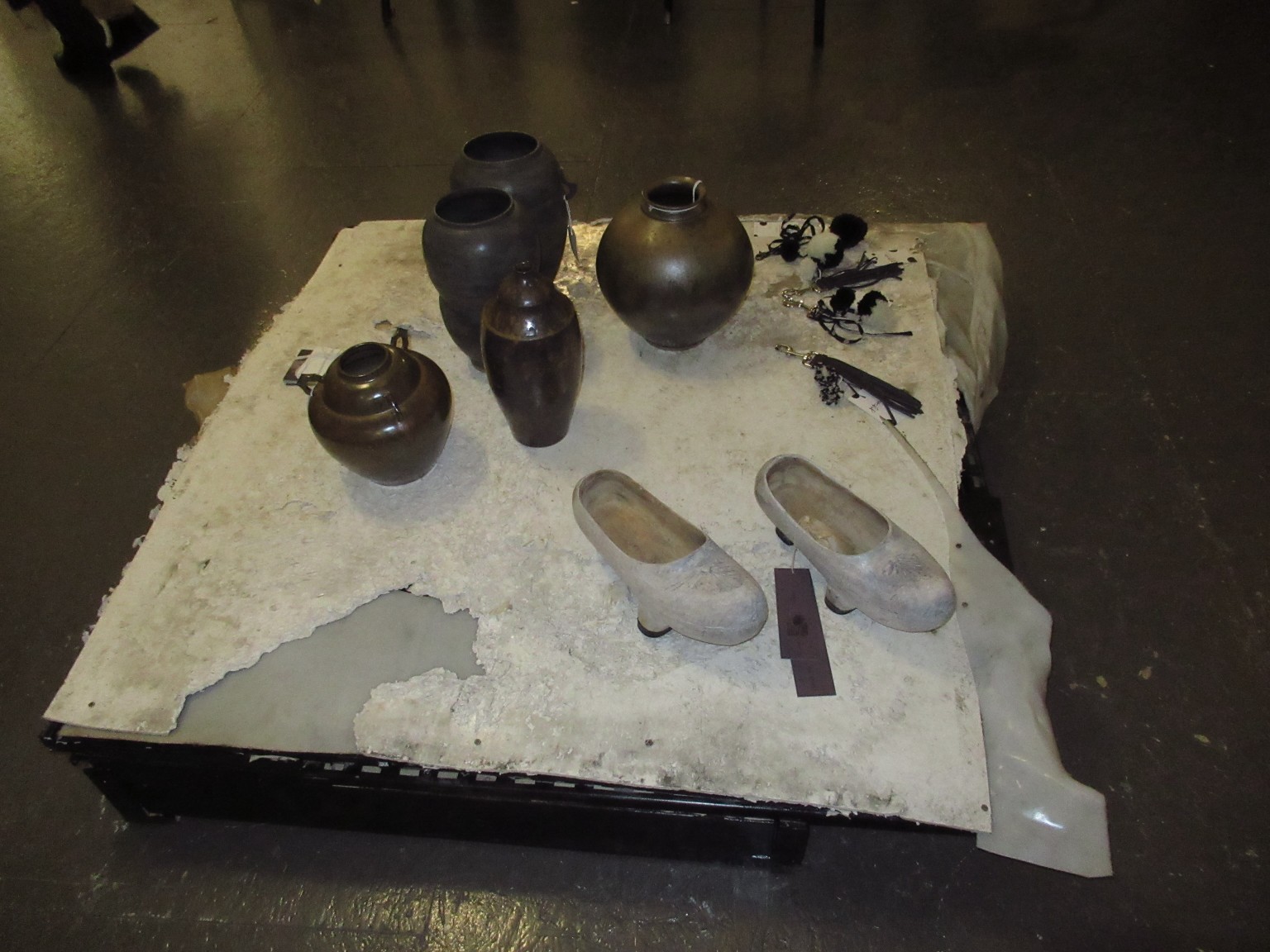 Céramiques, chaussures claires et accessoires sur une table sculpturale.