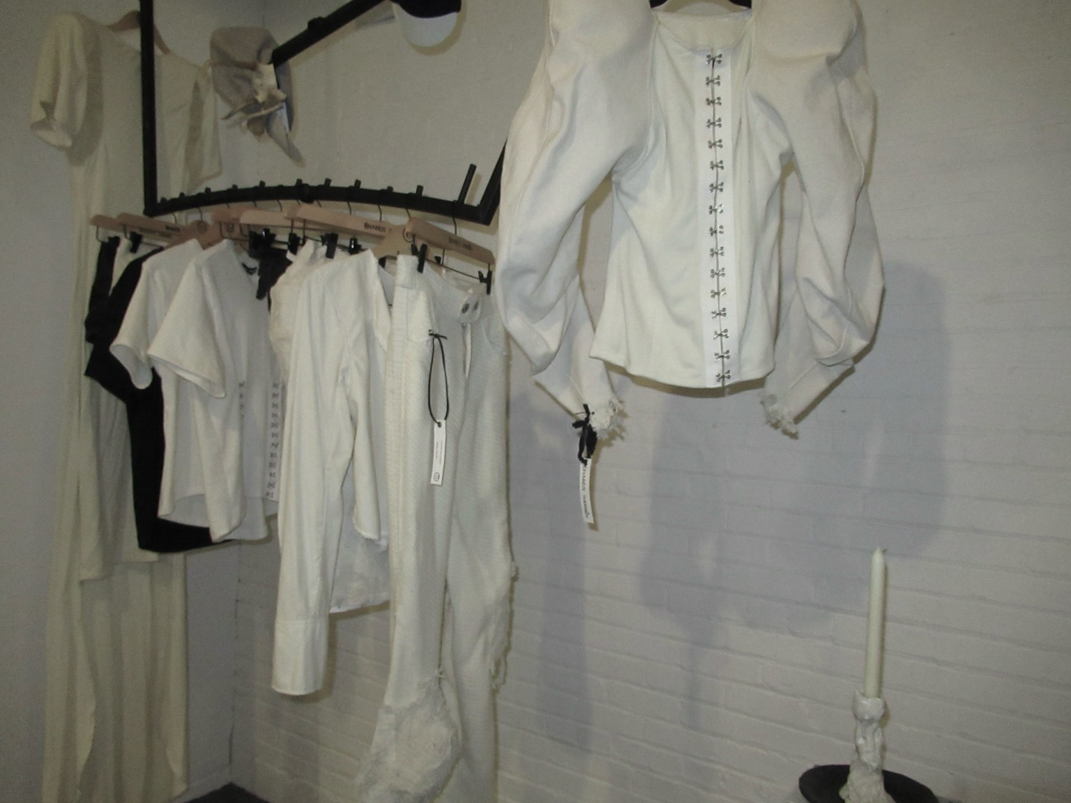 Vêtements blancs de créateurs indépendants sur un portant suspendu devant un mur de briques.